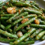 Din Tai Fung green beans on a white plate with chopsticks and minced garlic visible