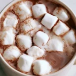 Hot cocoa in a white ceramic mug with whipped cream and cocoa powder dusted on top