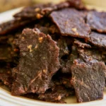 Deer jerky strips arranged on a white plate with visible black pepper seasoning and a dark brown glaze