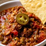 Instant Pot chili in a white bowl with shredded cheese, sour cream, and diced onions on top