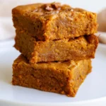 Pumpkin blondies cut into squares on a white plate with chocolate chips visible and a dusting of cinnamon