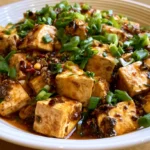 Mapo tofu in a white bowl with silky tofu cubes in glossy red chili sauce, garnished with sliced green onions