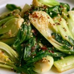 Garlic bok choy on a white plate with golden seared stems and dark green leaves, garnished with sesame seeds.