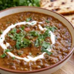 Dal makhani in a white bowl with a glossy butter finish, garnished with fresh cilantro and served with naan bread on the side