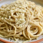 Cacio e pepe in a white bowl with creamy sauce coating spaghetti strands and black pepper visible on top