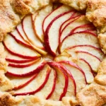Apple galette on a white plate with golden flaky crust folded over caramelized apple slices