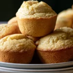 Cornbread muffins on a white plate with golden brown tops and visible cornmeal texture, butter and honey on the side